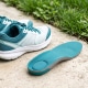 Gedämpfte Laufschuhe und orthopädische Einlage mit Fersenpolster auf Betonboden neben Rasen